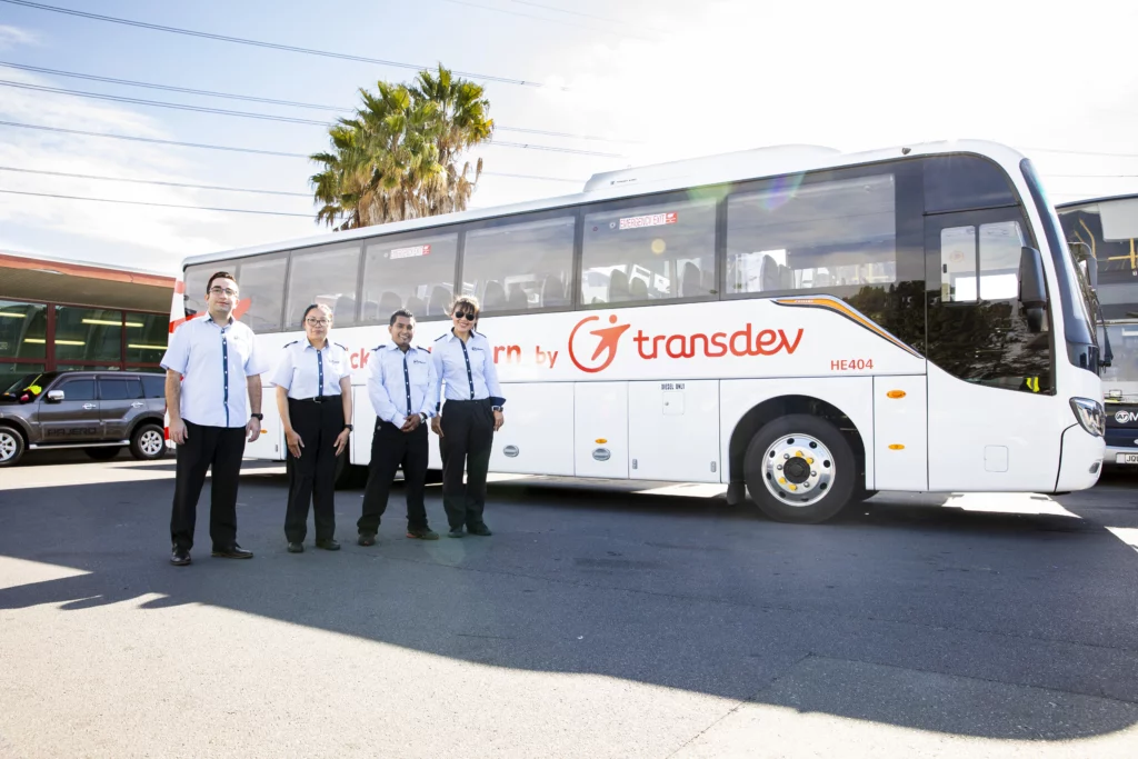 Four employees in white and black uniforms standing in front of a white bus.